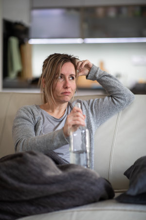 Midlle aged woman at home with a bottle of strong alcohol in her handsの写真素材