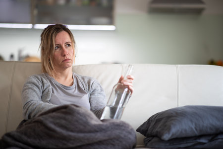 Midlle aged woman at home with a bottle of strong alcohol in her handsの写真素材