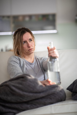 Midlle aged woman at home with a bottle of strong alcohol in her handsの写真素材
