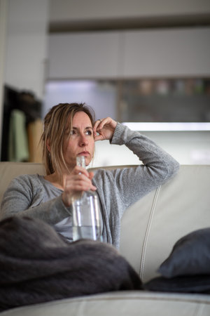 Midlle aged woman at home with a bottle of strong alcohol in her handsの写真素材