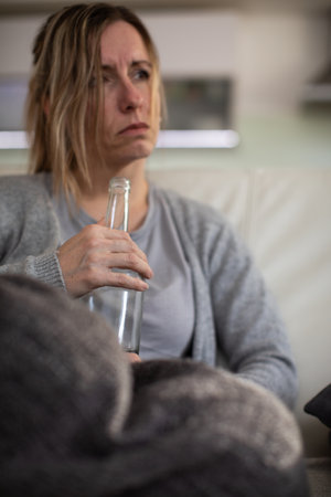 Midlle aged woman at home with a bottle of strong alcohol in her handsの写真素材