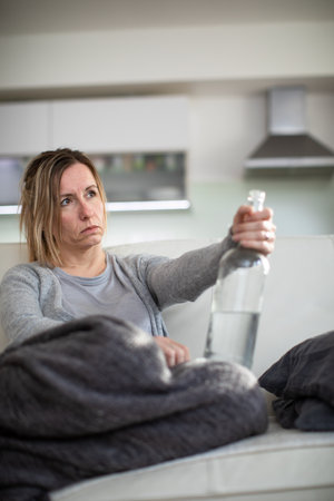 Midlle aged woman at home with a bottle of strong alcohol in her handsの写真素材