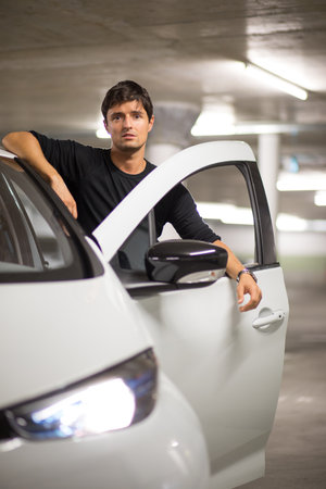 Underground parking/garage (shallow DOF; color toned image) - young male driver with his small city electric carの写真素材