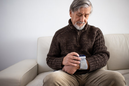 Senior man using medical device to measure blood pressure - elderly man suffering from high blood pressure sitting at home on sofa takes care of his healthの写真素材