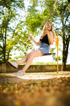 Carefree woman enjoying summer. Young woman is swinging on a swing in summer park garden.の写真素材