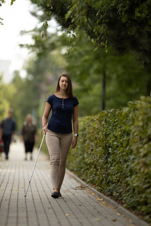 Young woman with vision impairment walking on city streets, using her white caneの写真素材