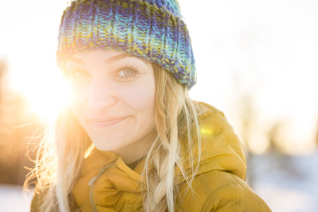 Winter portrait of a pretty, young woman bathing in warm evening sunlight in a snowy landscape.の写真素材