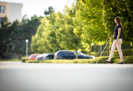 Young woman with vision impairment walking on city streets, using her white caneの写真素材