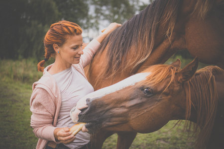 Pretty, young, redhead woman with her lovely horse, during her favorite leisureの写真素材