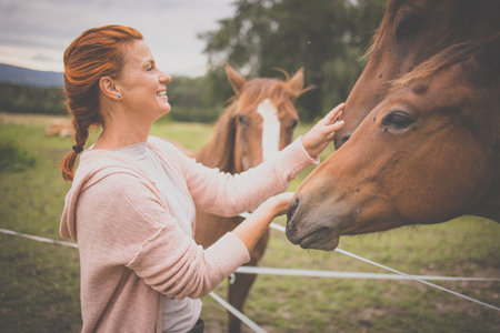 Pretty, young, redhead woman with her lovely horse, during her favorite leisureの写真素材