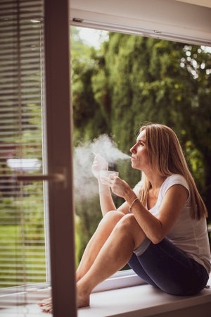 Mid-aged woman lighting a cigarette at home, getting her nicotine daily dose, unable to resist her unhealthy habitの写真素材