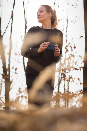 Young woman with binoculars outdoors on fall day. Enjoying the outdoors.の写真素材