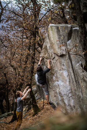 A rock climber climbing on a boulder rock outdoors. Group of friends involved in sports outside.の写真素材