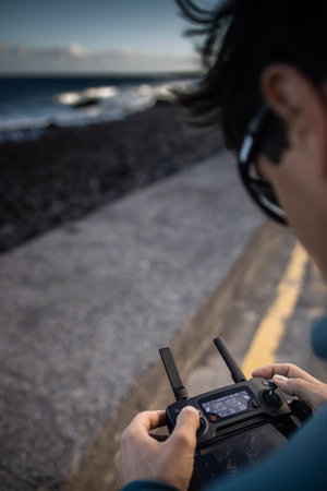Drone pilot in action, taking aerial photos and capturing footage of waves crashing on a beachの写真素材