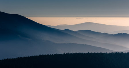 Mountain atmospheric landscape of high mountains in thick fog in rainy weather, panorama of mountain tops in thick clouds, dawn in the mountains in early spring.の写真素材