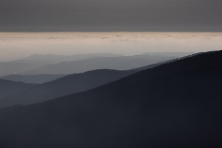 Mountain atmospheric landscape of high mountains in thick fog in rainy weather, panorama of mountain tops in thick clouds, dawn in the mountains in early spring.の写真素材