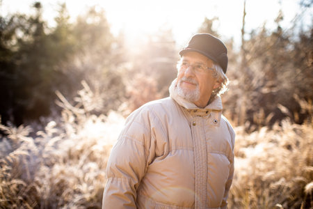 Happy senior man walking outside. Portrait of senior man in a forest on a winter day.の写真素材