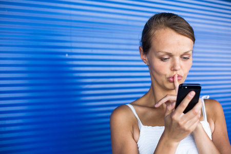 Portrait of a young woman sending a text message with a mobile phone against a blue backgroundの写真素材