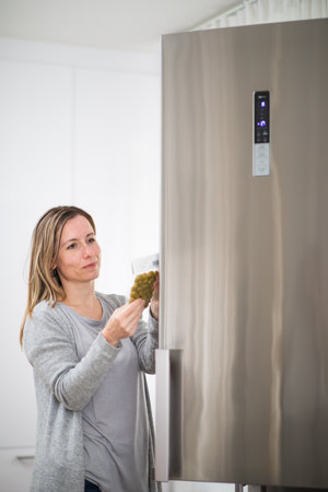 Pretty, middle-aged woman taking food out of the fridge, healthy food concept - expiry date concept