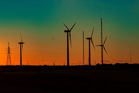 Wind turbines with orange green sunset and flock of birds.The alternative energy from the wind goes perfectly with the surrounding nature.の写真素材