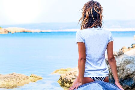 A girl with blonde hair in the foreground of shoulders with a white T-shirt observes the sea.の写真素材