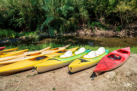 A set of ten old and worn kayak of various color on the riverside.の写真素材