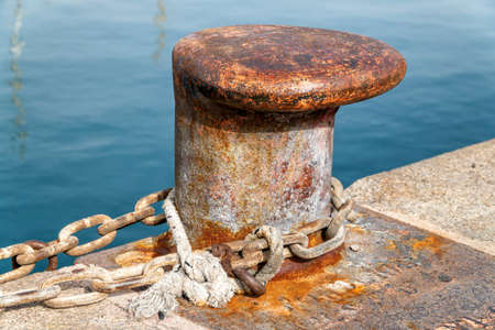 An old rusty marine bollard with nautical ropes along the quayside.