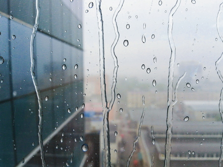 Rain drops on the window glass with skyscraper wall on the backgroundの写真素材