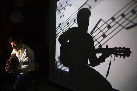 The guitar player is singing the song with a shadow of notes and silhouette of the guitarist on the...