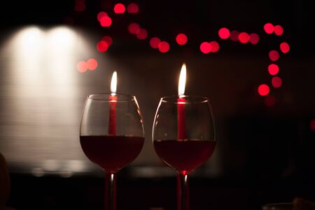 Romantic dinner: two glasses of wine and candels are in the dark with new year lights at the backgroundの写真素材