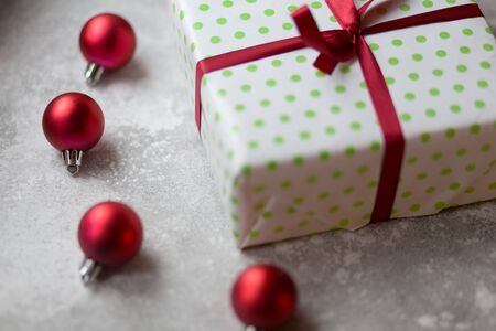 Christmas decorations on a gray background. A white and green box with a burgundy bow surrounded by unfocused burgundy Christmas balls, Christmas toys and stone ornament. Top view..の写真素材