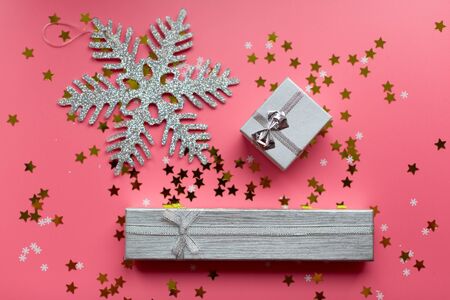 Silver snowflake and white textured gift boxes with ribbon bows surrounded by stars and snowflakes on a coral background, from above..の写真素材