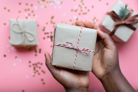 African woman hands holding present box with a bow on pastel pink background with stars and snowflakes confetti. Flat lay style..の写真素材