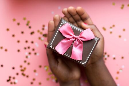 African woman hands holding present box with a bow on pastel pink background with stars and snowflakes confetti. Flat lay style..の写真素材