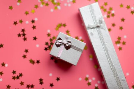 White textured gift boxes with ribbon bows surrounded by stars and snowflakes on a coral background, from above..の写真素材