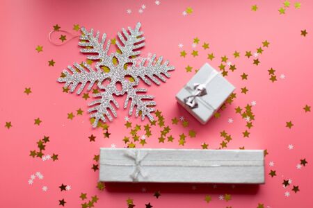 Silver snowflake and white textured gift boxes with ribbon bows surrounded by stars and snowflakes on a coral background, from above..の写真素材
