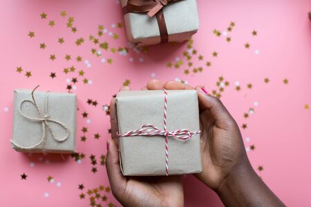 African woman hands holding present box with a bow on pastel pink background with stars and snowflakes confetti. Flat lay style..の写真素材