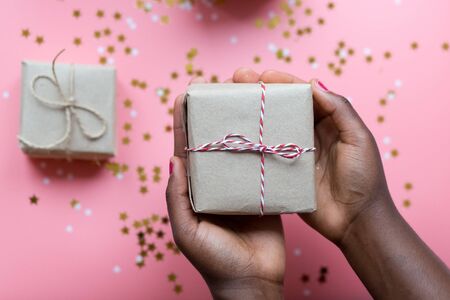 African woman hands holding present box with a bow on pastel pink background with stars and snowflakes confetti. Flat lay style..の写真素材