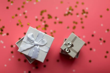 White textured gift boxes with ribbon bows surrounded by stars and snowflakes on a coral background, from above..の写真素材