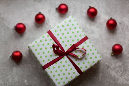 Christmas decorations on a gray background. A white and green box with a burgundy bow surrounded by unfocused burgundy Christmas balls, Christmas toys and stone ornament. Top view..の写真素材