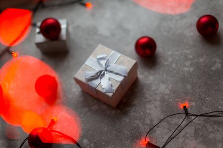 Christmas decorations on a gray background. A white with a bow is surrounded by unfocused burgundy Christmas balls, Christmas toys and red garland..の写真素材
