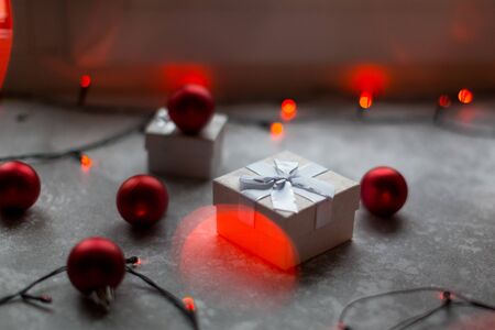 Christmas decorations on a gray background. A white with a bow is surrounded by unfocused burgundy Christmas balls, Christmas toys and red garland..の写真素材