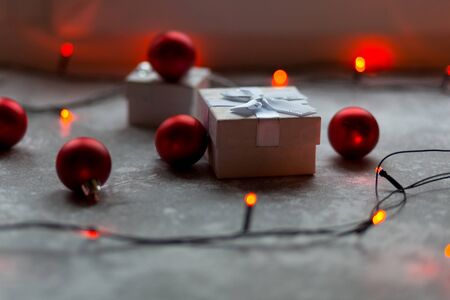 Christmas decorations on a gray background. A white with a bow is surrounded by unfocused burgundy Christmas balls, Christmas toys and red garland..の写真素材