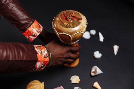 Hands of an African man in national clothes holds djembe drum surrounded by seashellsの写真素材