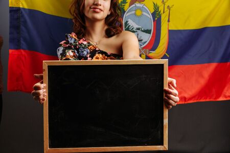 Portrait of young Latin American woman student holding an empty chalkboard before the Ecuadorian flag..の写真素材