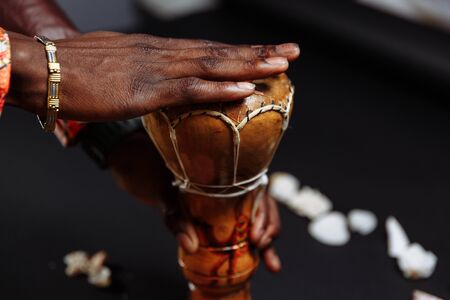 Hands of an African man in national clothes holds djembe drum surrounded by seashellsの写真素材