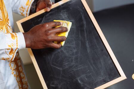 Hand in national clothes holding brush erase on black chalkboard and cleaning it