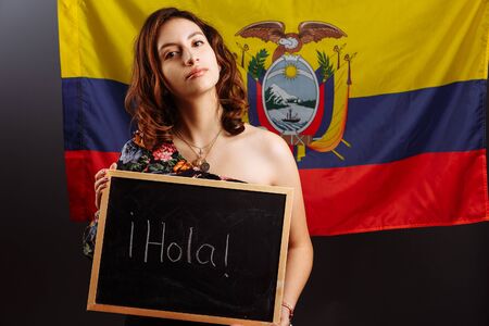 Portrait of young Latin American woman student holding a chalkboard with Hello word on her native...