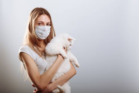 Yound lady in protective surgical mask holds cat pet. Coronavirus disease COVID-19 is dangerous for petsの写真素材