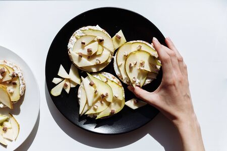 The woman hand holding the delicious tartlets or cake with mixed pieces of apples and pears and chocolate from above. Summer pastry desserts.の写真素材